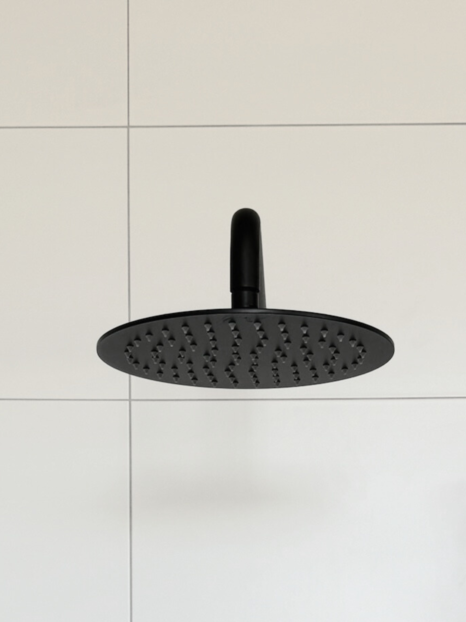 A black rain shower head with white tiles 