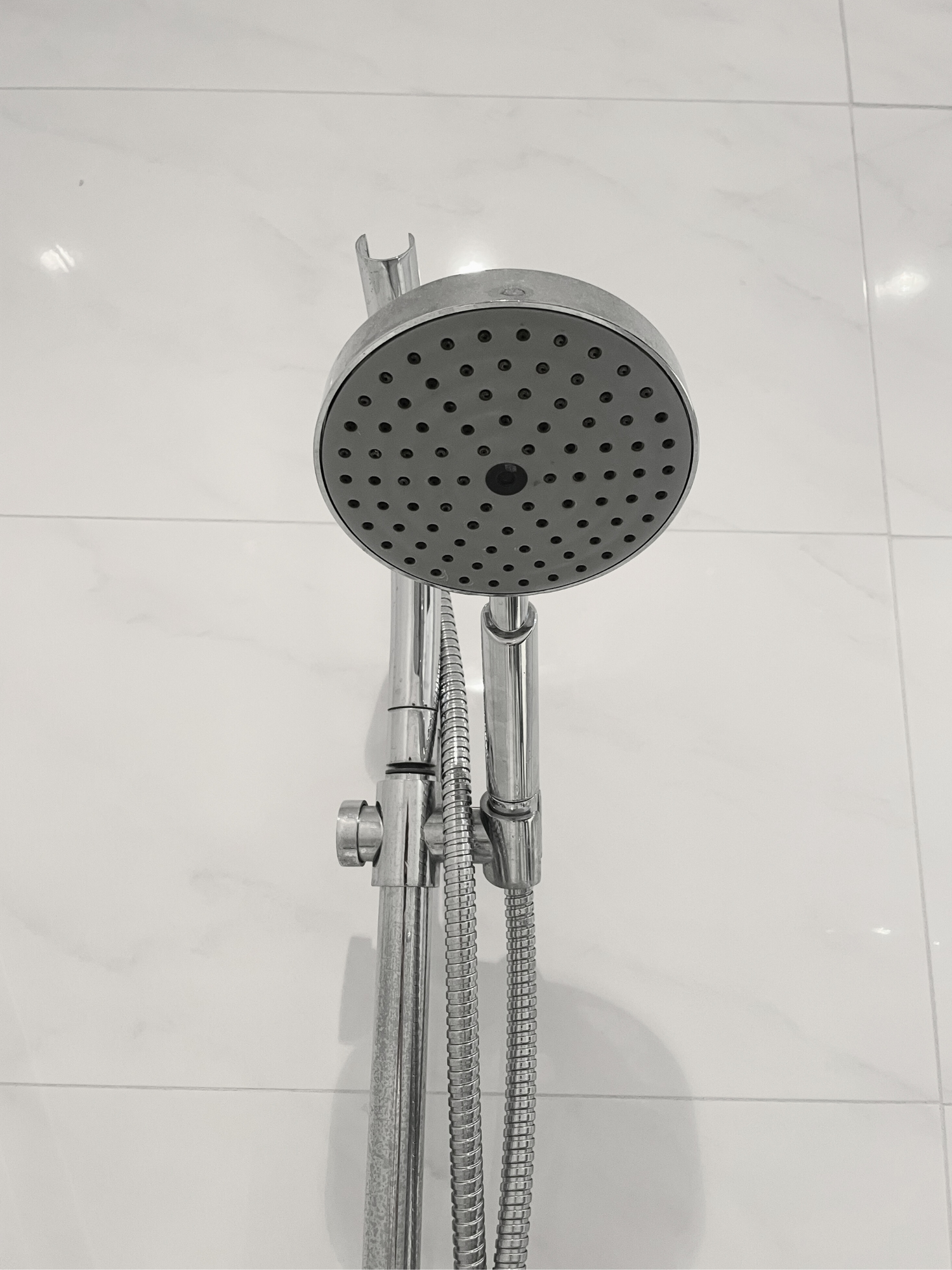 A handheld shower with white tiles 