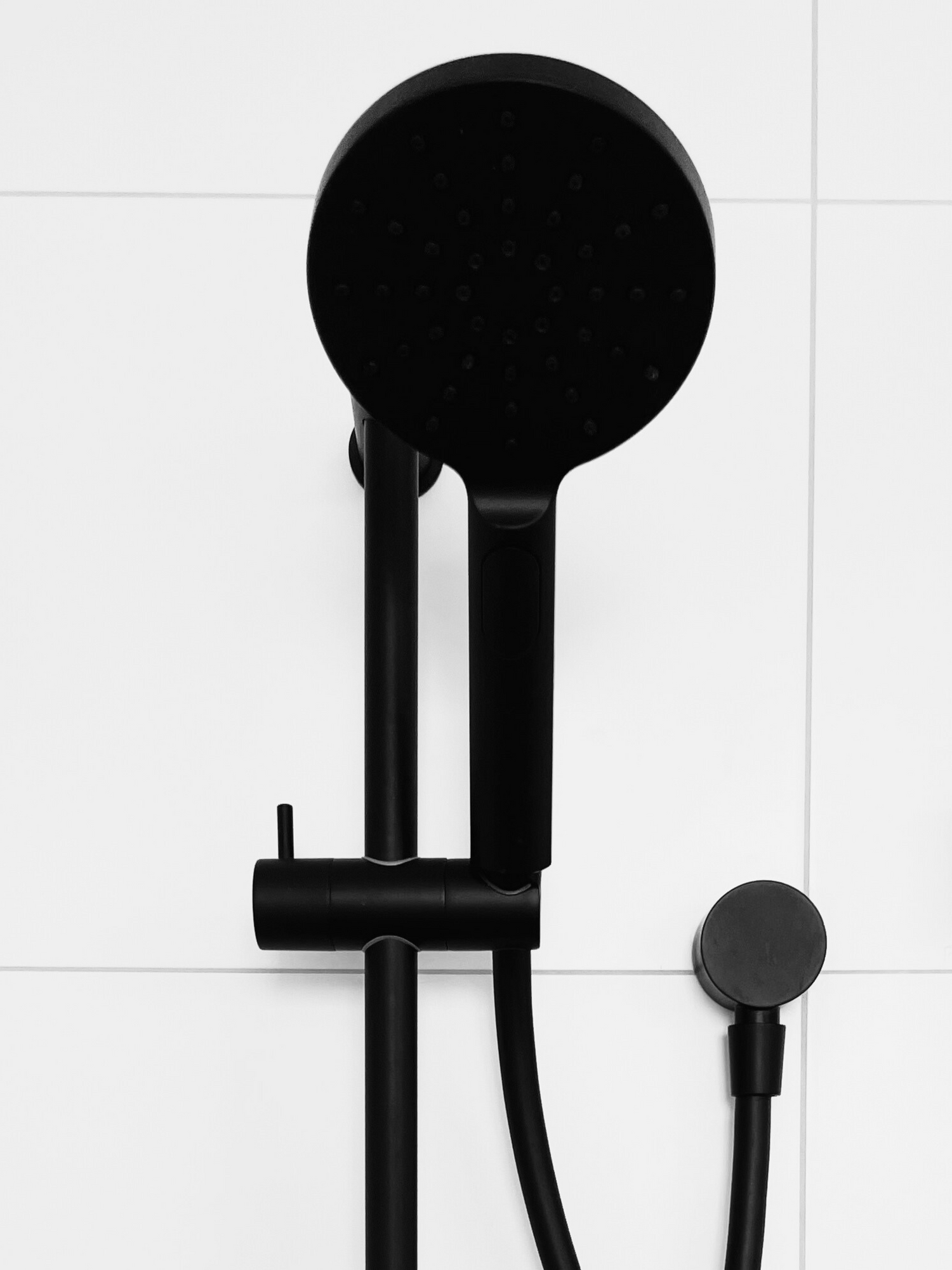 A black handheld shower head with white tiles